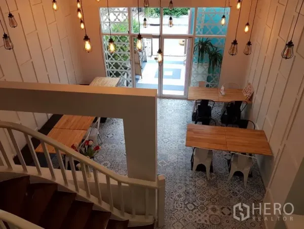 Retail Space for rent in Bang Rak, Bangkok - Double-height retail interior with pendant lights, wooden tables, patterned floor tiles and a glass front entrance seen from the staircase.