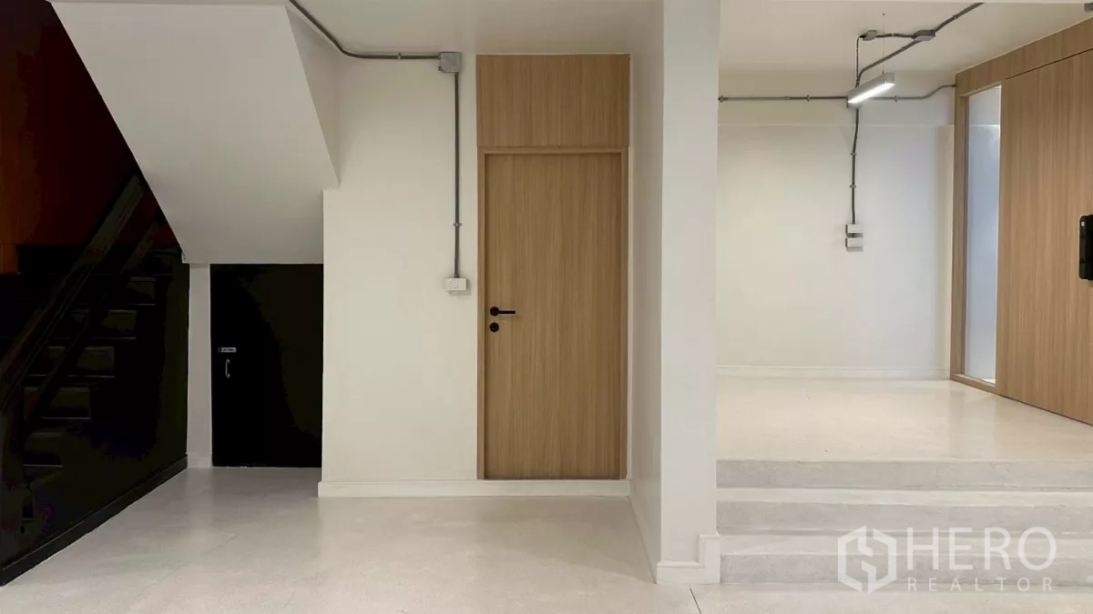 Home Office for rent in Watthana, Bangkok - Ground floor lobby with wooden doors, exposed conduits and staircase under-stairs storage.