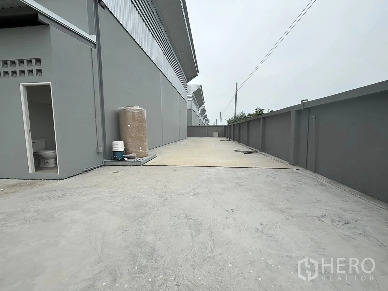 Factory for rent or sale in Bang Bo, Samut Prakan - Rear concrete service yard with perimeter wall and side access door beside the factory.