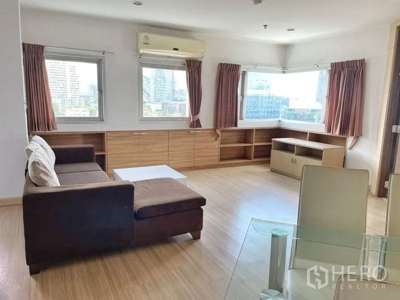 Condominium for rent in Khlong Toei, Bangkok - Corner living room with wraparound windows, built-in shelving and city views.