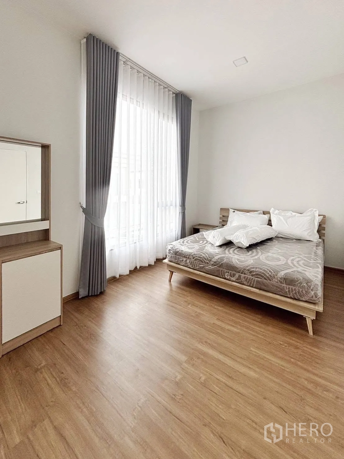 ทาวน์เฮาส์ for rent in Bang Phli, Samut Prakan - ห้องนอนสว่าง เตียง ผ้าม่านสูงจรดเพดาน พื้นไม้ และโต๊ะเครื่องแป้ง