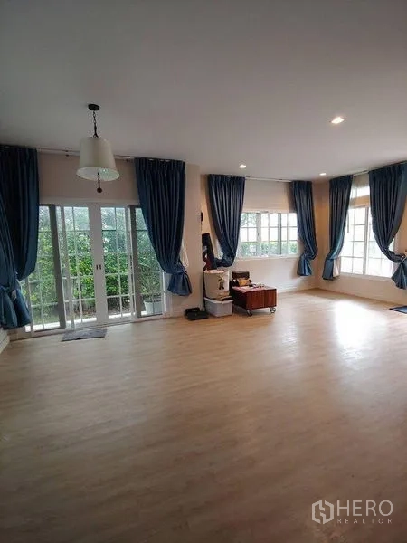 独立式住宅 出售在Khlong Sam Wa, Bangkok - 大客厅，法式落地门与转角窗，蓝色窗帘，面向花园。