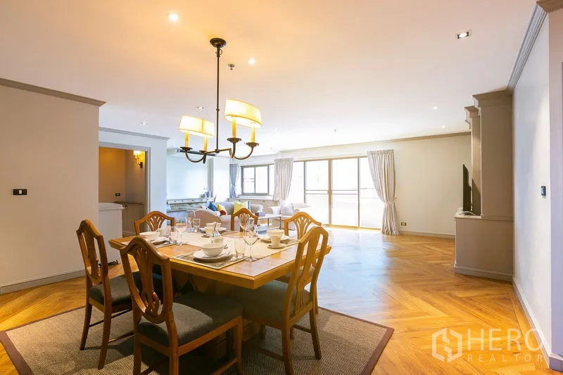 Apartment for rent in Watthana, Bangkok - Dining area with six-seat wooden table under pendant lights, opening to the living room.