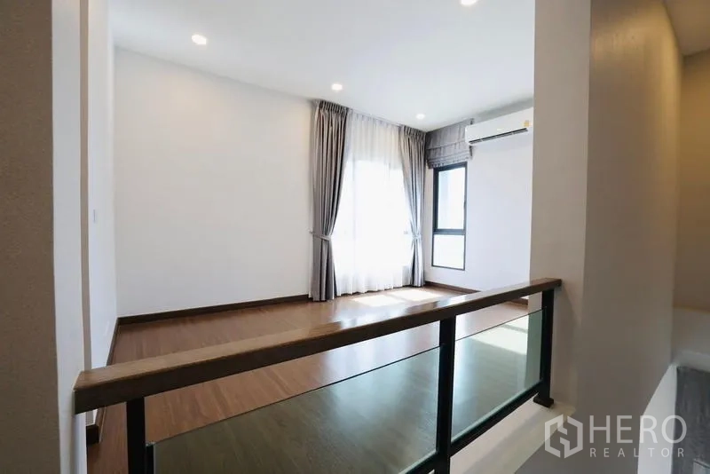 独立式住宅 出租在Bang Phli, Samut Prakan - 二楼走廊，木地板与玻璃栏杆，采光充足。