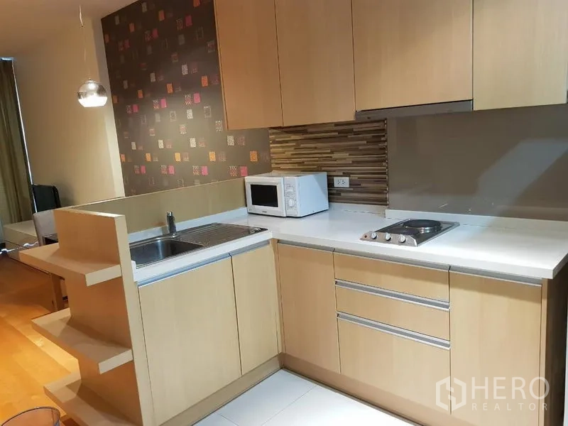 公寓 出租在Ratchathewi, Bangkok - 紧凑厨房，浅木柜体，水槽，电灶，微波炉与拼贴挡板。