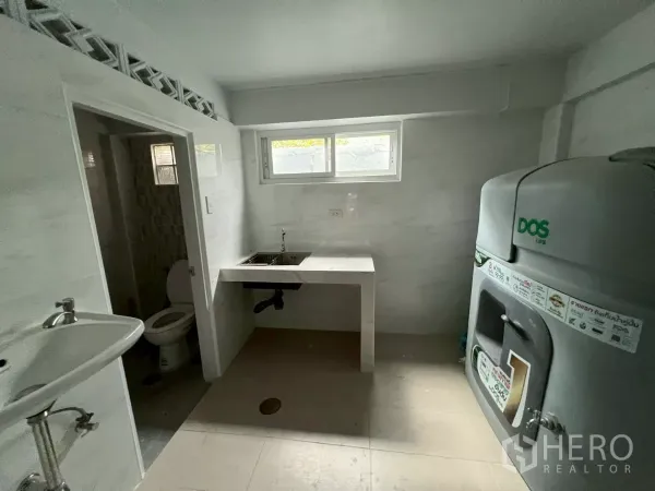 Shophouse for rent in Khlong Toei, Bangkok - Utility room with a countertop sink, small window, toilet door and large DOS water tank.