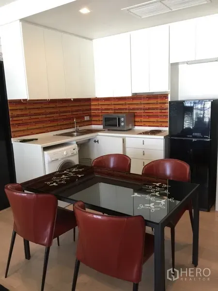 Condominium for rent in Watthana, Bangkok - Modern open kitchen with white cabinets, orange tile backsplash, glass dining table, washing machine and black fridge in a Thonglor condo.