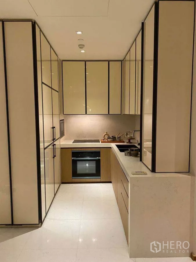 Condominium for rent or sale in Khlong Toei, Bangkok - U‑shaped kitchen with built‑in cabinets, electric hob, oven and light stone countertops.