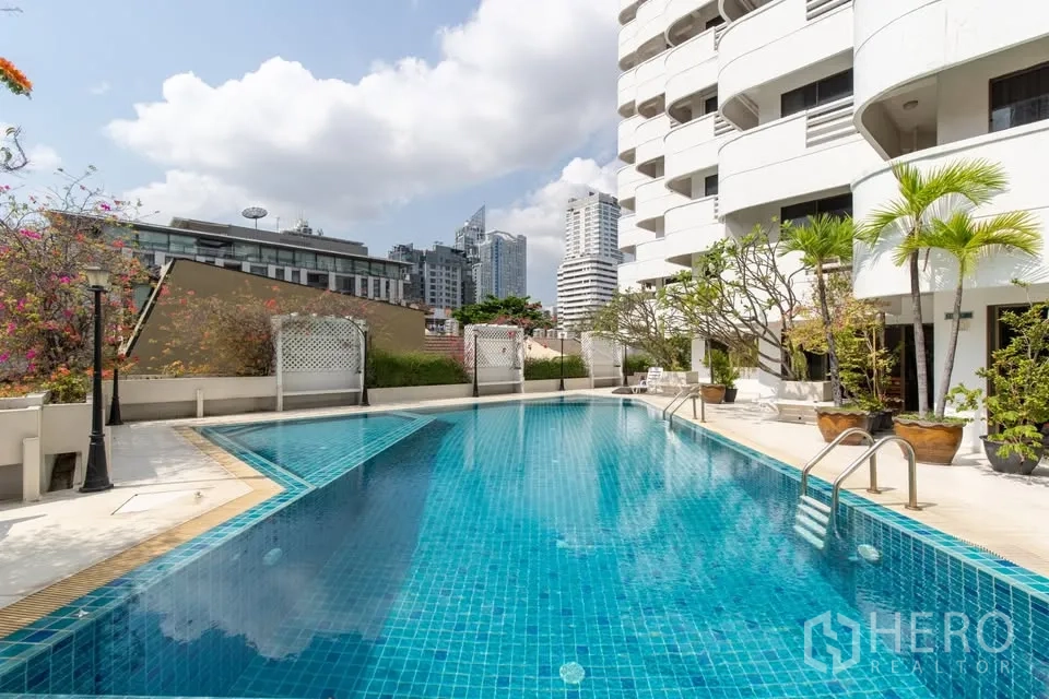 公寓 for rent in Watthana, Bangkok - 户外游泳池毗邻白色公寓楼，可眺望城市天际线。