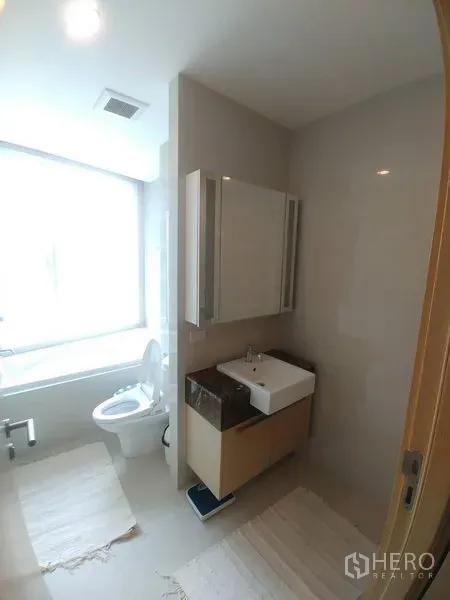 Condominium for rent or sale in Watthana, Bangkok - Bright bathroom with bathtub, vanity sink, and mirrored cabinet.