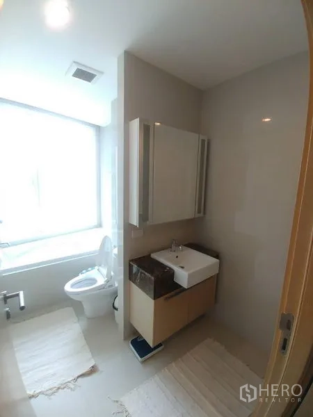 Condominium for rent or sale in Watthana, Bangkok - Bright bathroom with bathtub, vanity sink, and mirrored cabinet.