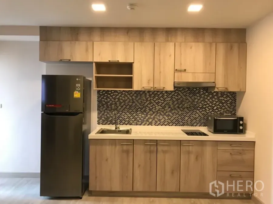Condominium for rent in Watthana, Bangkok - Fitted kitchen with wood cabinetry, mosaic tile backsplash, cooktop, sink, microwave, and refrigerator.