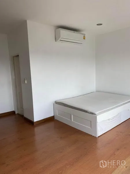 Townhouse for rent in Lat Phrao, Bangkok - Third bedroom with built-in air conditioner and platform bed on wood floors.