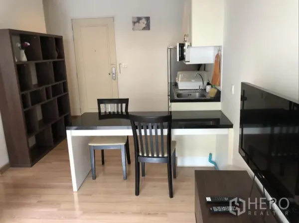 Condominium for rent in Pathum Wan, Bangkok - Open-plan dining and living area with wall-mounted TV, shelving unit and two-seat table.