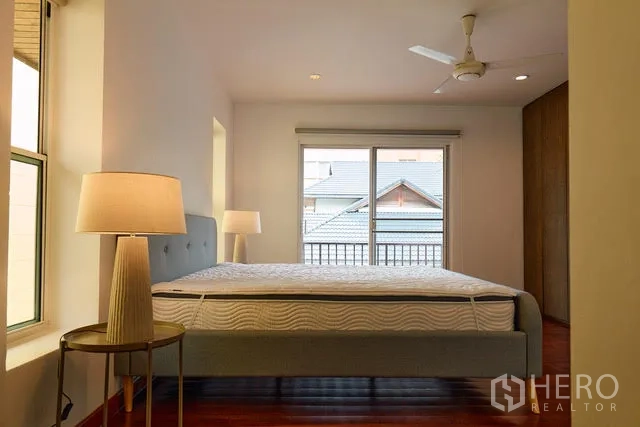 Detached House for rent in Watthana, Bangkok - Bedroom with balcony access, wardrobe and bedside lamps.