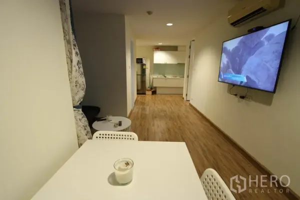Condominium for rent or sale in Wang Thonglang, Bangkok - Open-plan living space with dining table, wall-mounted TV, and kitchen at the far end.