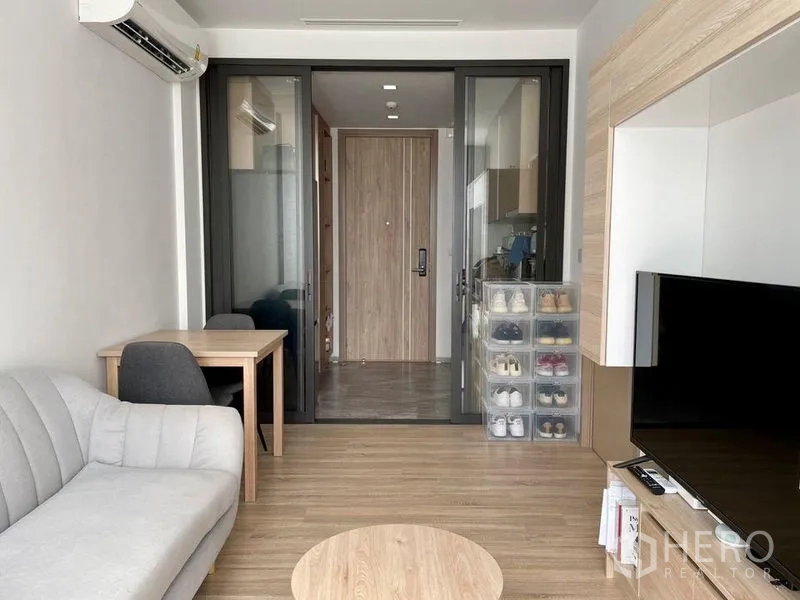 公寓 出租或出售在Watthana, Bangkok - 起居区配沙发与餐桌，玻璃隔断连接玄关与厨房。