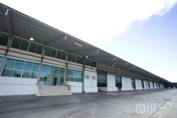 Warehouse for rent in Si Racha, Chon Buri - Modern warehouse exterior with long covered loading dock, glass-front office and multiple roller doors.