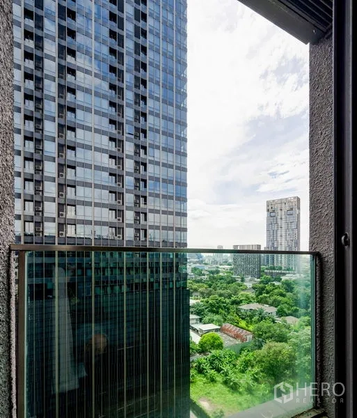 Condominium for sale in Khlong Toei, Bangkok - Balcony with glass railing facing modern high-rise buildings and a green cityscape.