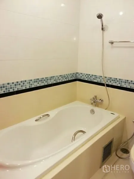 Condominium for rent in Khlong Toei, Bangkok - Bathroom with built-in bathtub, handheld shower and mosaic tile border.