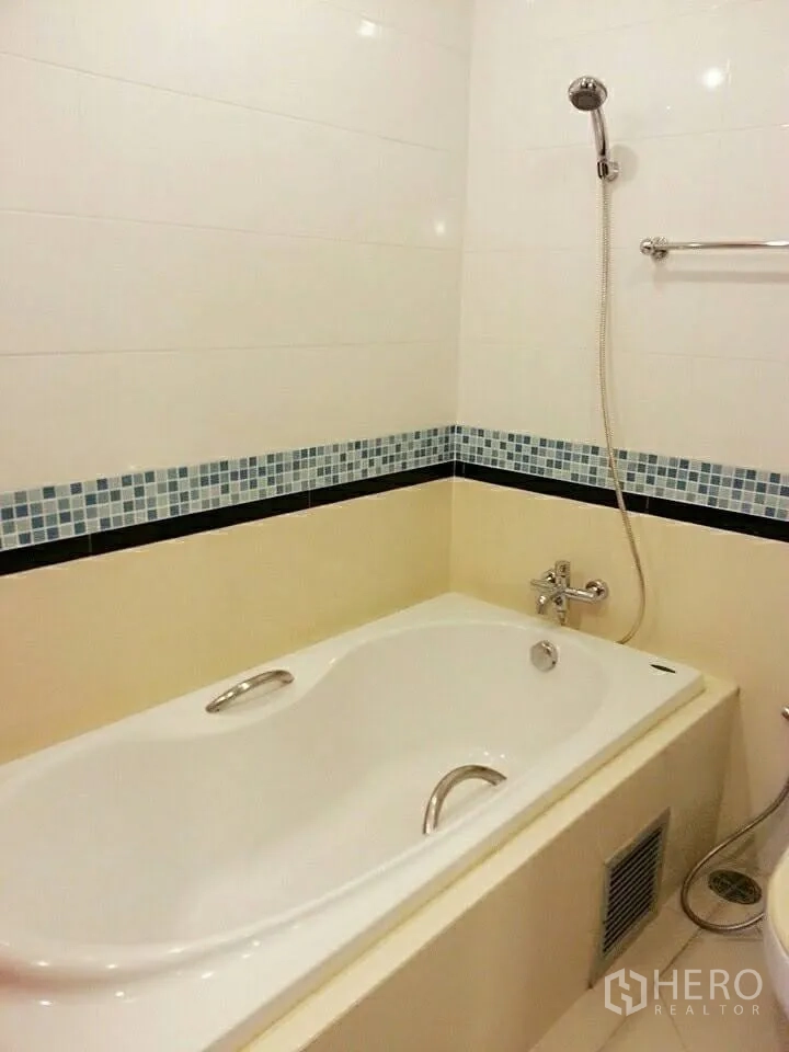 Condominium for rent in Khlong Toei, Bangkok - Bathroom with built-in bathtub, handheld shower and mosaic tile border.