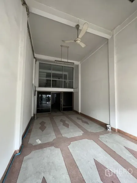 Shophouse for rent in Phra Khanong, Bangkok - Long, open-plan retail space with tall white walls, suspended light and decorative tiles leading to glass doors.