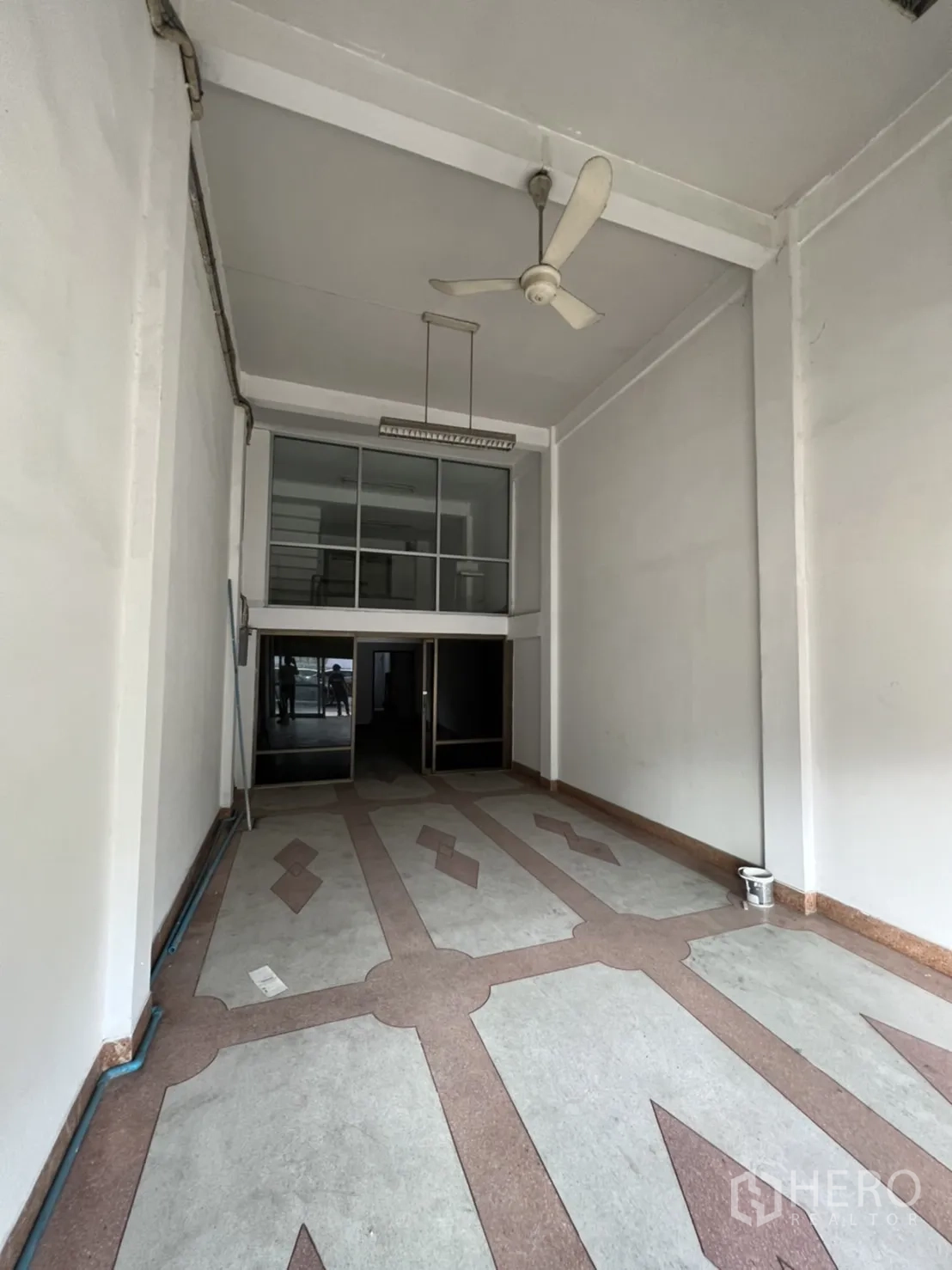 Shophouse for rent in Phra Khanong, Bangkok - Long, open-plan retail space with tall white walls, suspended light and decorative tiles leading to glass doors.