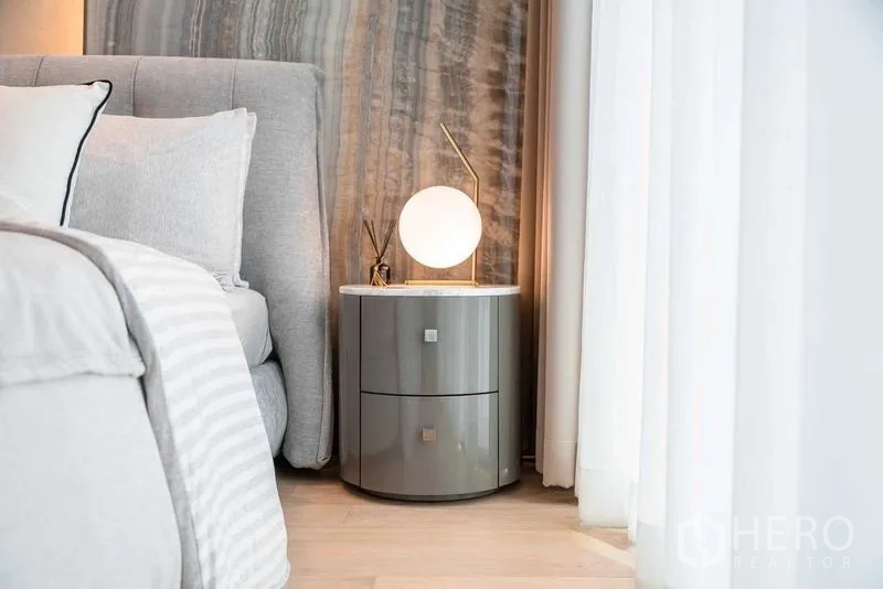 Condominium for rent or sale in Pathum Wan, Bangkok - Modern round bedside table with globe lamp beside flowing curtains.