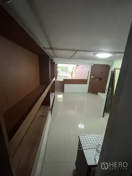Shophouse for rent in Khlong Toei, Bangkok - Long interior corridor with wall-mounted wooden shelves and tile flooring.