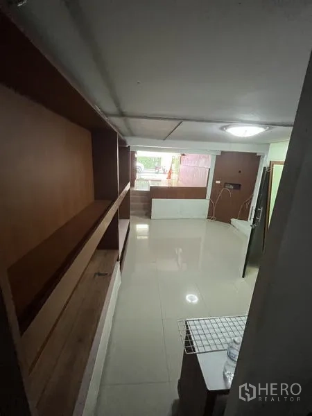 Shophouse for rent in Khlong Toei, Bangkok - Long interior corridor with wall-mounted wooden shelves and tile flooring.