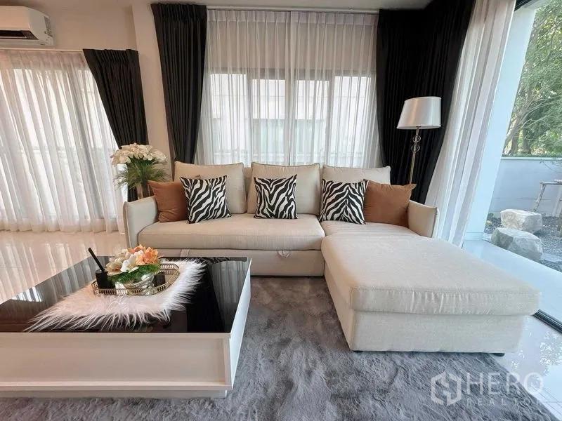 Detached House for rent or sale - Stylish lounge with L-shaped beige sofa, zebra cushions and glossy coffee table by wide windows.