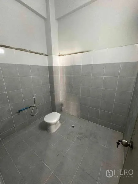 货栈 出租在Samut Sakhon - 仓库内灰色瓷砖卫生间，配坐便器和喷枪。