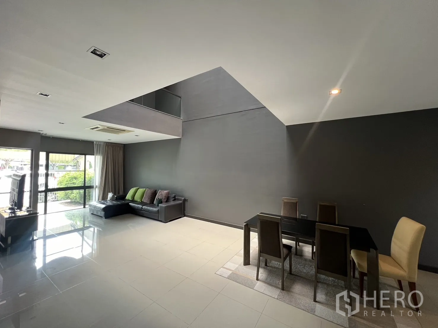 Townhouse for rent in Lat Phrao, Bangkok - Open-plan lounge and dining room with mezzanine void, glossy tile floors and sliding glass doors.