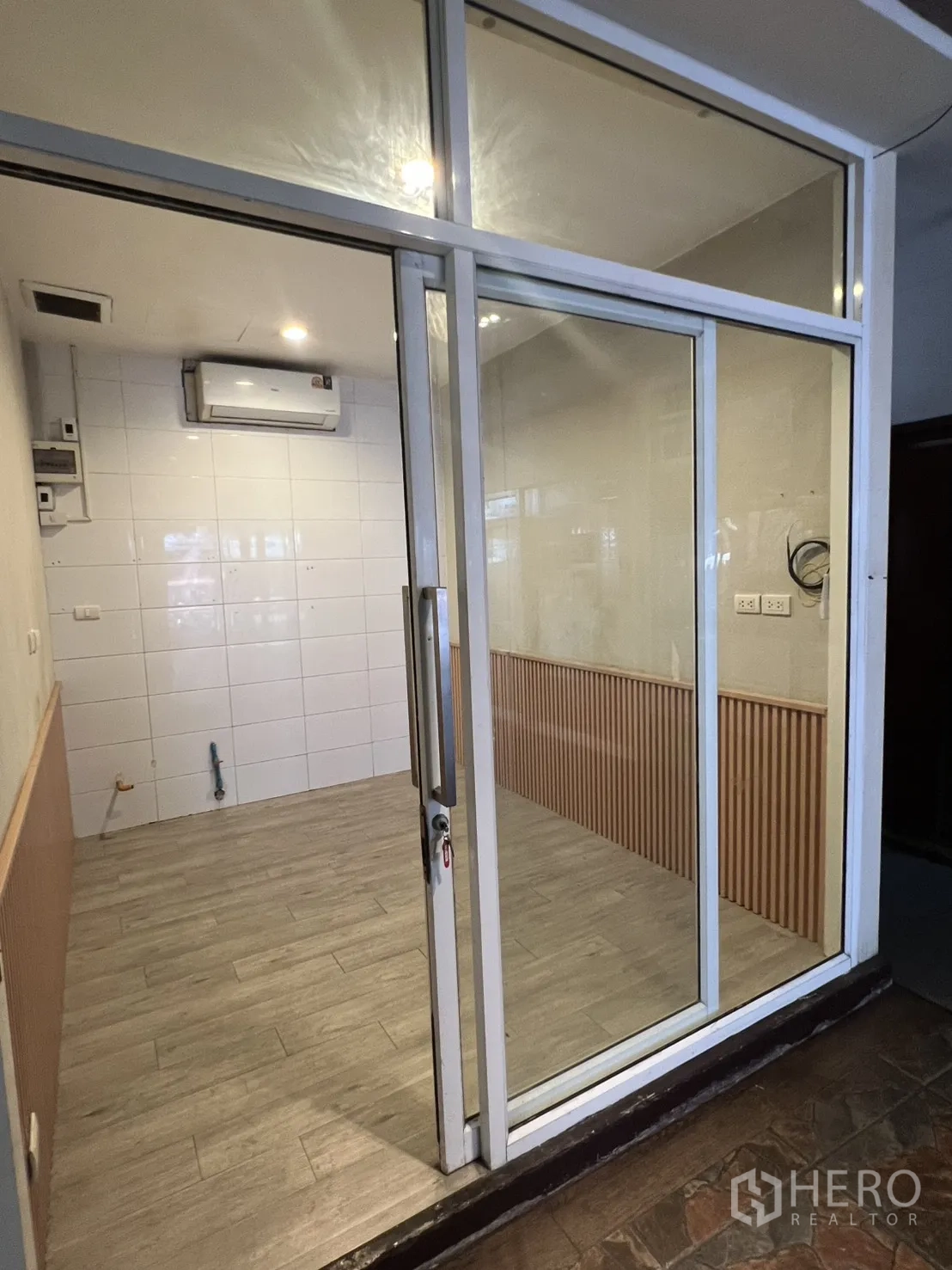 Retail Space for rent in Watthana, Bangkok - Compact 8 sqm retail unit with glass sliding storefront, wood-look tile floor, white tiled wall, and air conditioner in Sukhumvit.
