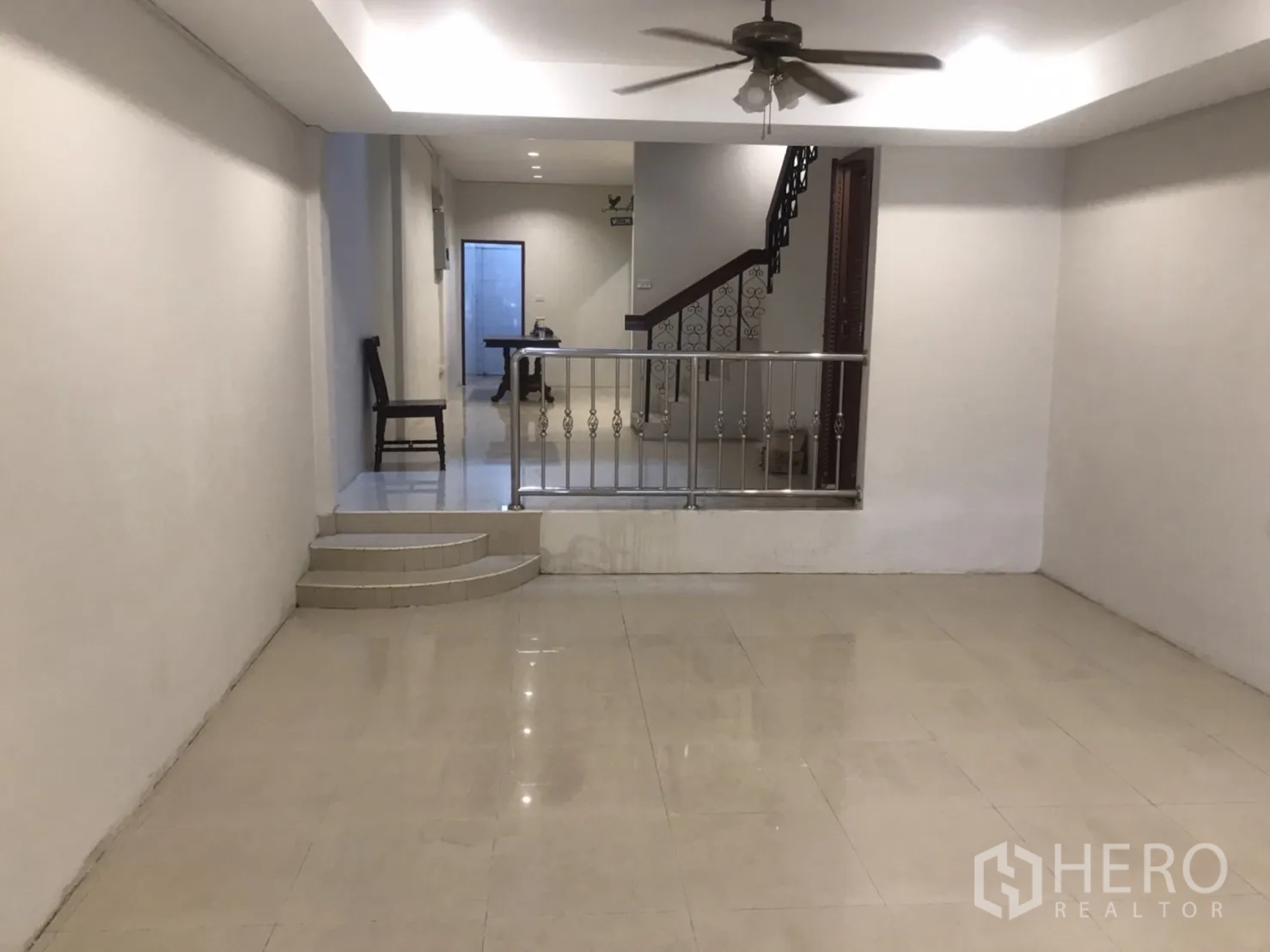 Home Office for rent in Khlong Toei, Bangkok - Spacious ground-floor living area with glossy tile floors, ceiling fan, and split-level steps with a metal railing.