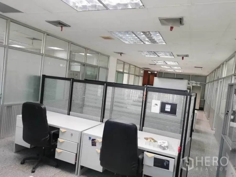 办公空间 出租在Bang Na, Bangkok - 设有隔断屏风与转椅的工位区，顶置荧光灯，玻璃隔间布局。