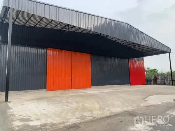 Warehouse for rent in Khan Na Yao, Bangkok - Modern black metal warehouse exterior with large orange sliding doors and a covered loading area in Khan Na Yao, Bangkok.