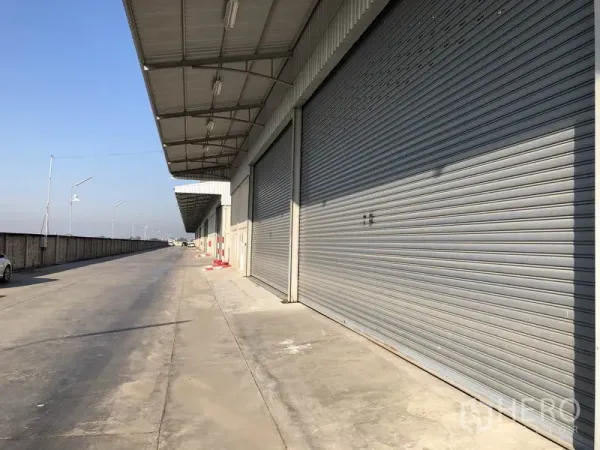 Warehouse for rent in Lam Luk Ka, Pathum Thani - Row of large electric roller shutter doors beneath a long canopy with easy truck access.