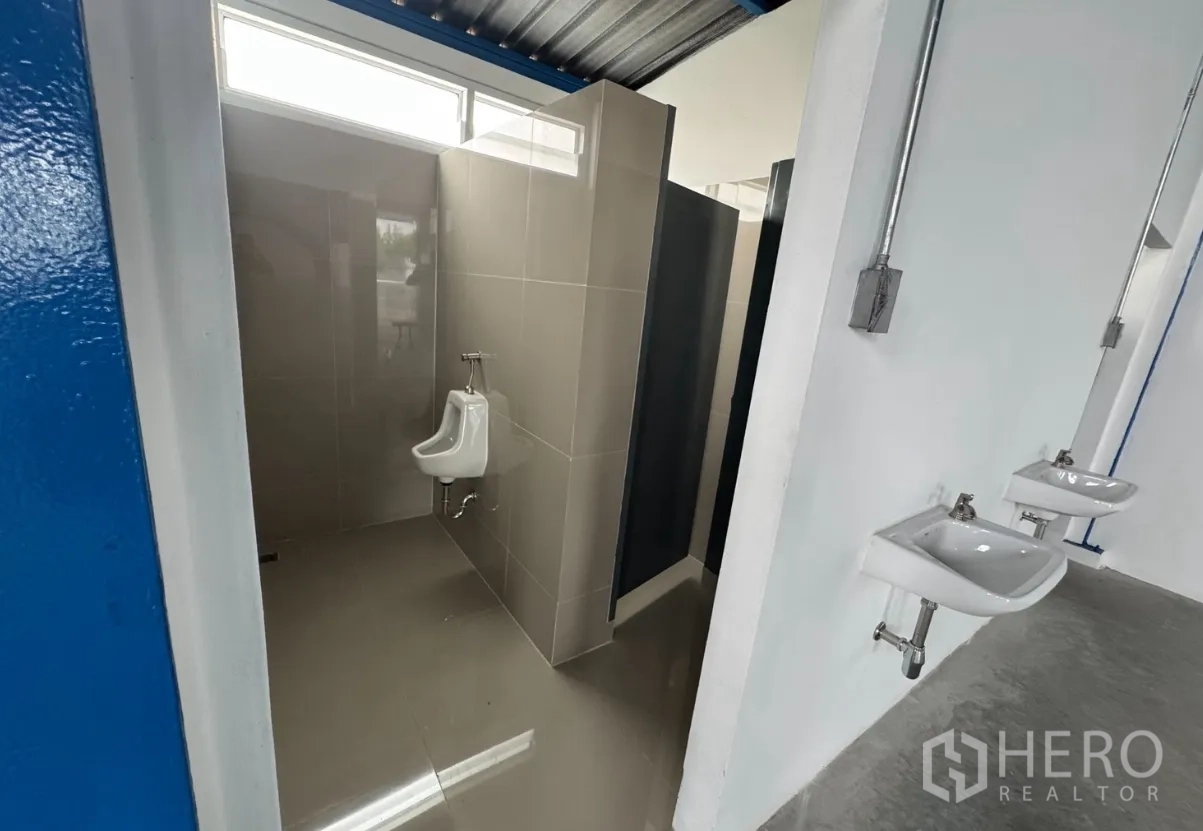 Warehouse for rent in Lam Luk Ka, Pathum Thani - Tiled restroom with a urinal, private stalls, and wall-mounted sinks.