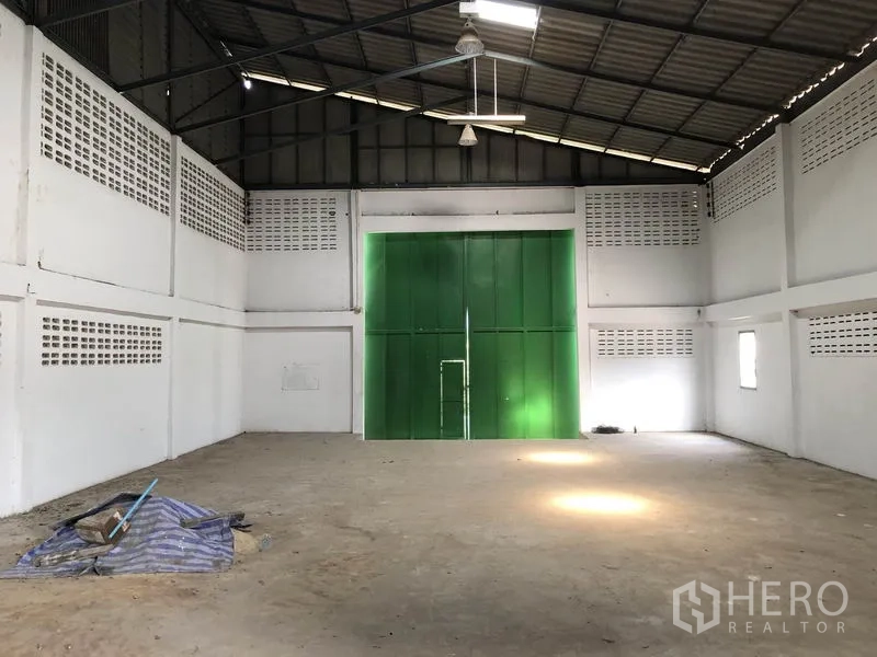 货栈 出租或出售在Khlong Luang, Pathum Thani - 空置仓库面向超大绿色钢门，顶部装有吊扇与工业照明。