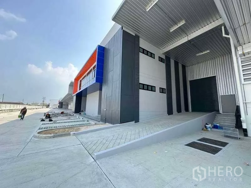 货栈 出租在Chon Buri - 保税区现代仓库外观，带有遮雨装卸坡道和彩色立面。