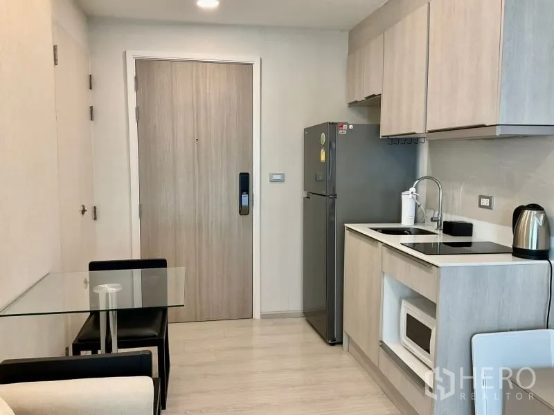 Condominium for sale in Khlong Toei, Bangkok - Compact kitchenette with light wood cabinets, cooktop, fridge and microwave by the entry.