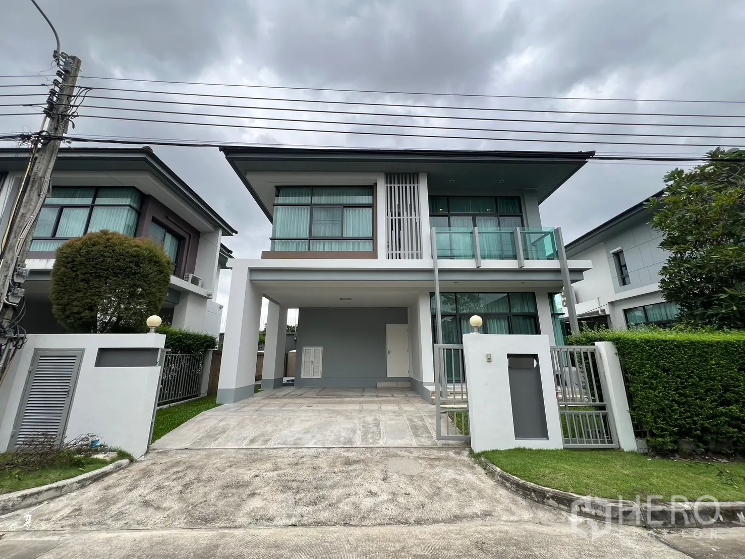 Detached House for rent in Bang Kapi, Bangkok - Modern two-storey detached house with glass balcony, gated driveway and hedges under a cloudy sky in Bang Kapi.