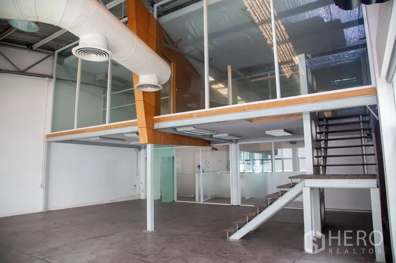 Warehouse for rent in Prawet, Bangkok - Mezzanine office block with glass walls, exposed ducts and stair access inside the industrial warehouse.