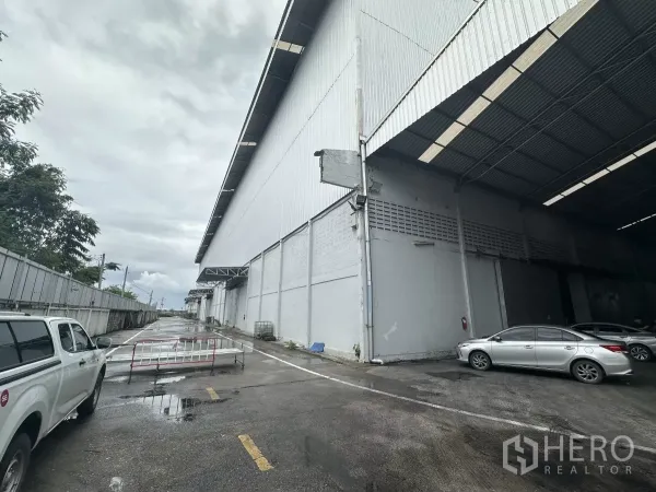 Warehouse for rent in Mueang Pathum Thani, Pathum Thani - Exterior of large industrial warehouse with covered loading bay, wide driveway and on-site parking in Pathum Thani.