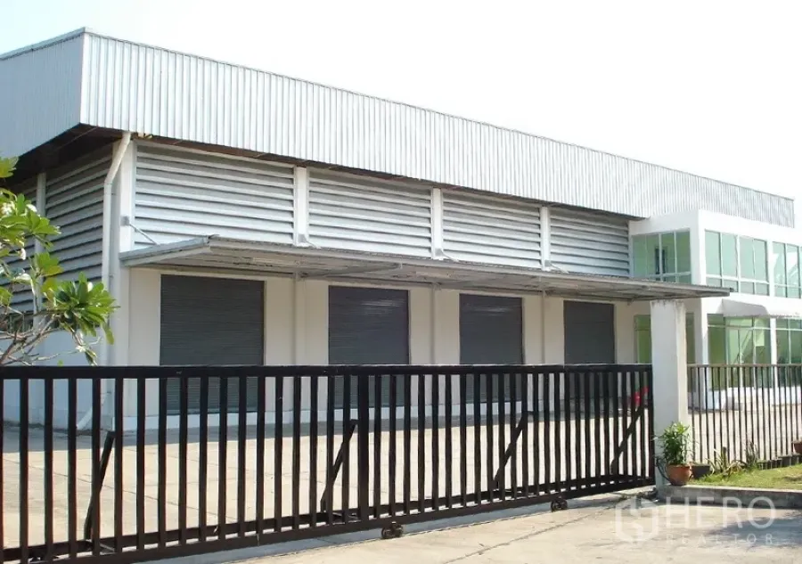 Warehouse for rent in Samut Prakan - Gated warehouse exterior with multiple roller shutter doors, canopy and louvered ventilation in Bang Phli.