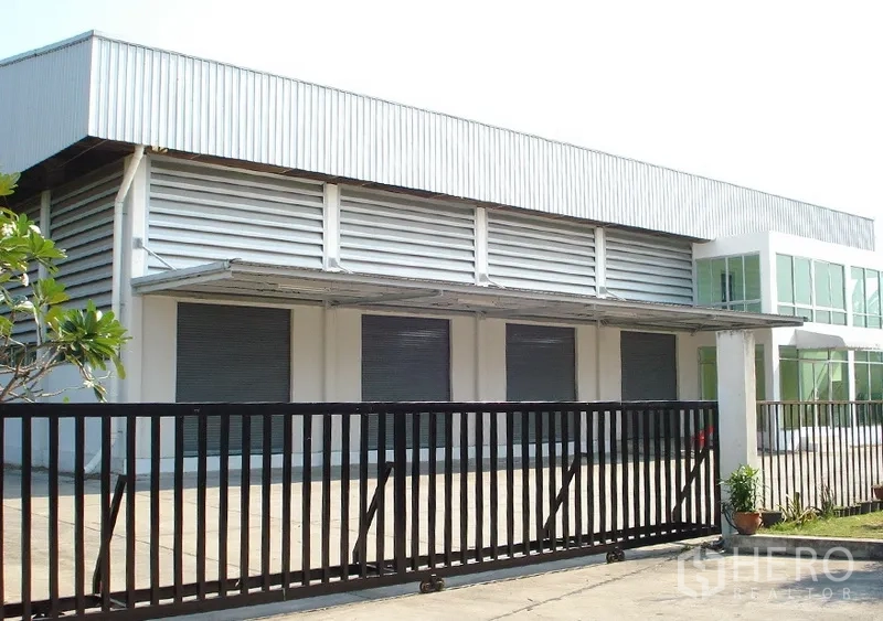 Warehouse for rent in Samut Prakan - Gated warehouse exterior with multiple roller shutter doors, canopy and louvered ventilation in Bang Phli.