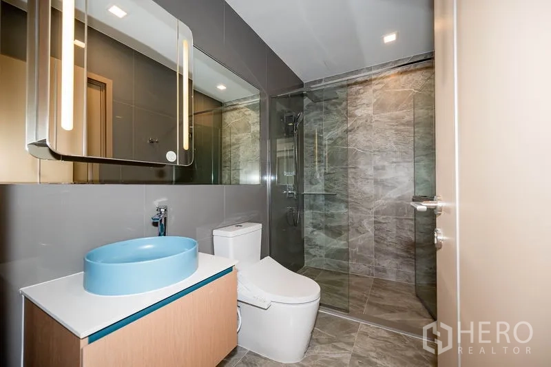 Condominium for rent in Watthana, Bangkok - Modern bathroom with blue basin, glass shower and gray stone tiles.