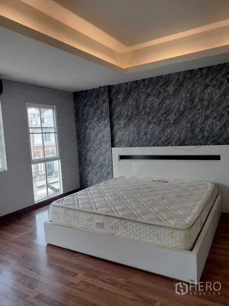 Townhouse for rent in Bueng Kum, Bangkok - Corner bedroom with large windows, cove lighting and a white bed frame.