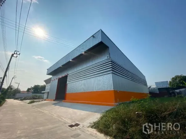 货栈 出租在Don Mueang, Bangkok - 带橙色裙墙的钢结构仓库转角视图，配置坡道通行的安静道路。